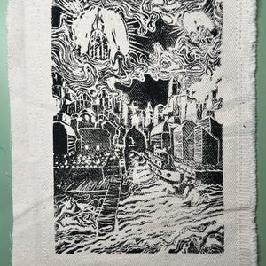 Könnte beinhalten: Schwarz-Weiß-Linolschnitt, der eine Stadtlandschaft mit Gebäuden, Wasser und wirbelnden Wolken darstellt. Das Kunstwerk befindet sich auf einem rechteckigen Stück weißem Stoff mit ausgefranstem Rand, was einen strukturierten und künstlerischen Look erzeugt.