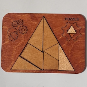 May include: Wooden puzzle with a geometric design. The puzzle pieces form a triangle shape. The wooden base is rectangular with the word "PUZZLE" and a gear graphic. Additional graphics include a person's profile and gears.