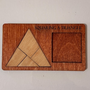 Puede incluir: Rompecabezas de madera con el texto "SQUARING A TRIANGLE". El rompecabezas presenta un triángulo hecho de cuatro piezas y un recorte cuadrado. La madera tiene una mancha marrón rojiza, y las piezas son de un tono más claro.