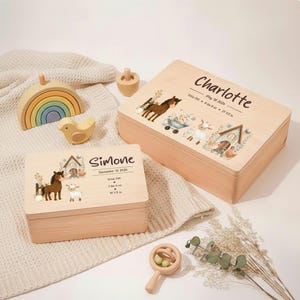 May include: Two wooden keepsake boxes with farm animal illustrations and personalized names. One box is labeled "Simone" with birth details. Other wooden toys include a rainbow, bird, and rattle.