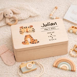 May include: A light wooden keepsake box with a cartoon tiger illustration. The box is personalized with the name "Julian", birthdate, time, weight (6 lbs 7 oz), and length (18 3/4 in). Other baby toys are in the image.