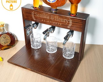 May include: A dark brown wooden liquor dispenser with three spouts, three glasses, and three bottles. The dispenser is engraved with "Semira & Henry" and "05.07.2025". The bottles are filled with amber liquid. The image also includes a bottle of Cool Creek XO.