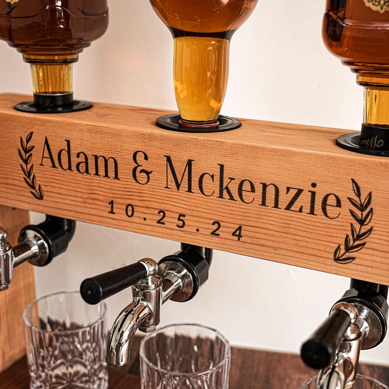 May include: A wooden liquor dispenser with three spouts and glass bottles. The wooden beam is engraved with "Adam & McKenzie" and the date "10.25.24". The dispenser has a rustic design, with a natural wood finish and black accents.