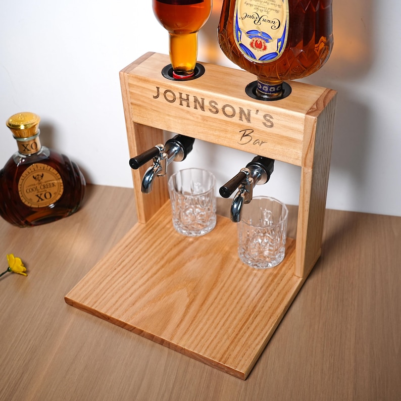 May include: Wooden liquor dispenser with two spouts, two glasses, and two bottles of liquor. The dispenser is engraved with "JOHNSON'S Bar". The bottles are filled with amber-colored liquor.
