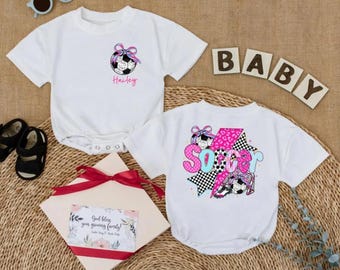 May include: Two white baby onesies with soccer-themed graphics. One features a soccer ball with a bow and the name "Hailey." The other has the word "SOCCER" in pink, blue, and black. Accessories include sunglasses, shoes, and a gift box.