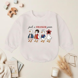 May include: White baby onesie with the text "just a STRANGER goose" and four cartoon geese dressed as characters. The geese are wearing a blue jacket, a red vest, a sailor outfit, and a flower. A fun, whimsical design.