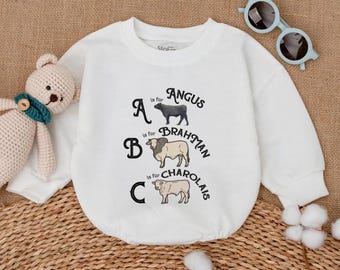May include: White baby onesie with the text "A is for Angus, B is for Brahman, C is for Charolais" and illustrations of each breed. A light blue pair of sunglasses and a stuffed bear are next to the onesie.