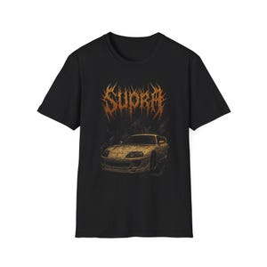 Könnte beinhalten: Schwarzes T-Shirt mit einer goldfarbenen Grafik eines Autos und dem Wort "Supra" in einer stilisierten Schriftart. Die Autografik ist detailliert, und der Text hat ein einzigartiges, kantiges Design. Das Shirt besteht aus einem weichen Material.