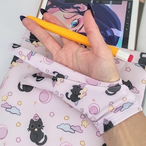 May include: A light pink tablet sleeve with a repeating pattern of black cats, clouds, stars, and moons. A yellow stylus rests on the tablet, which displays a digital art project. The sleeve is designed to hold a tablet.