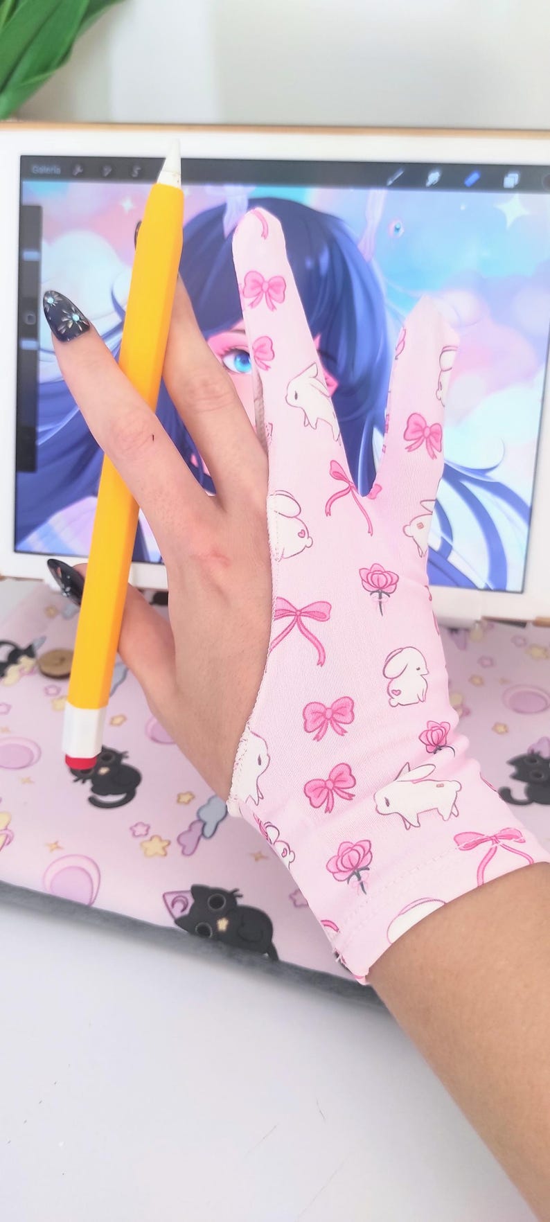 May include: Pink drawing glove with a pattern of white bunnies, pink bows, and roses. A yellow stylus is held in the glove. The glove is designed for digital art and drawing on a tablet. The background includes a tablet displaying digital art.