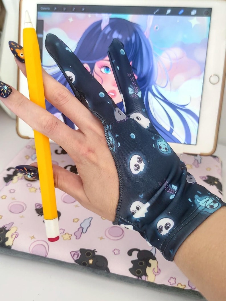May include: A dark blue artist's glove with a pattern of white ghost and butterfly illustrations. A yellow stylus with a white tip is held in the glove. The glove is designed for digital art and drawing on a tablet.