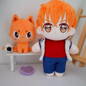 May include: A plush doll of a character with orange hair, wearing a red shirt, blue shorts, and a white jacket. Beside it is an orange cat plush on a white bench, and a small white and black plush. A purple heart-shaped item is on the floor.