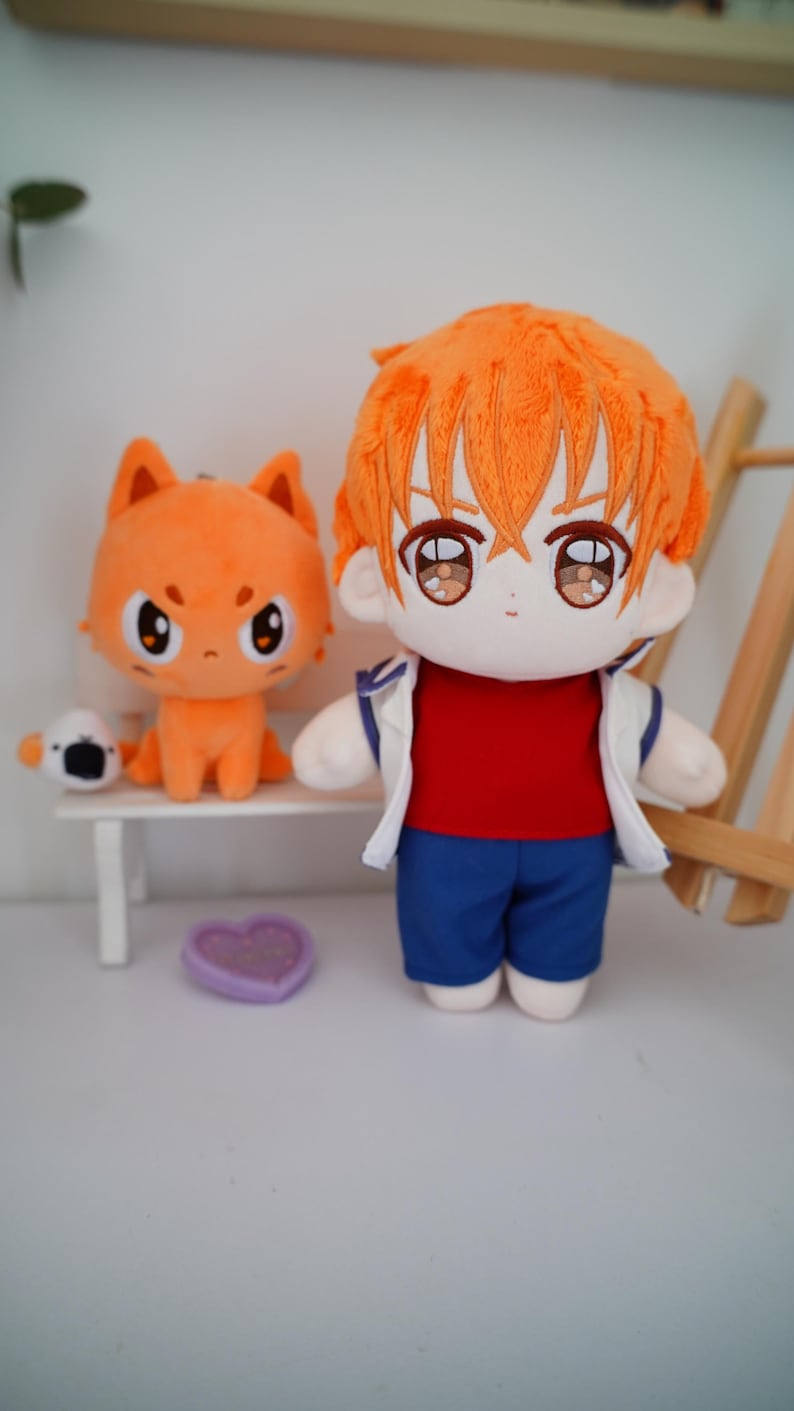 May include: A plush doll of a character with orange hair, wearing a red shirt, blue shorts, and a white jacket. Beside it is an orange cat plush on a white bench, and a small white and black plush. A purple heart-shaped item is on the floor.