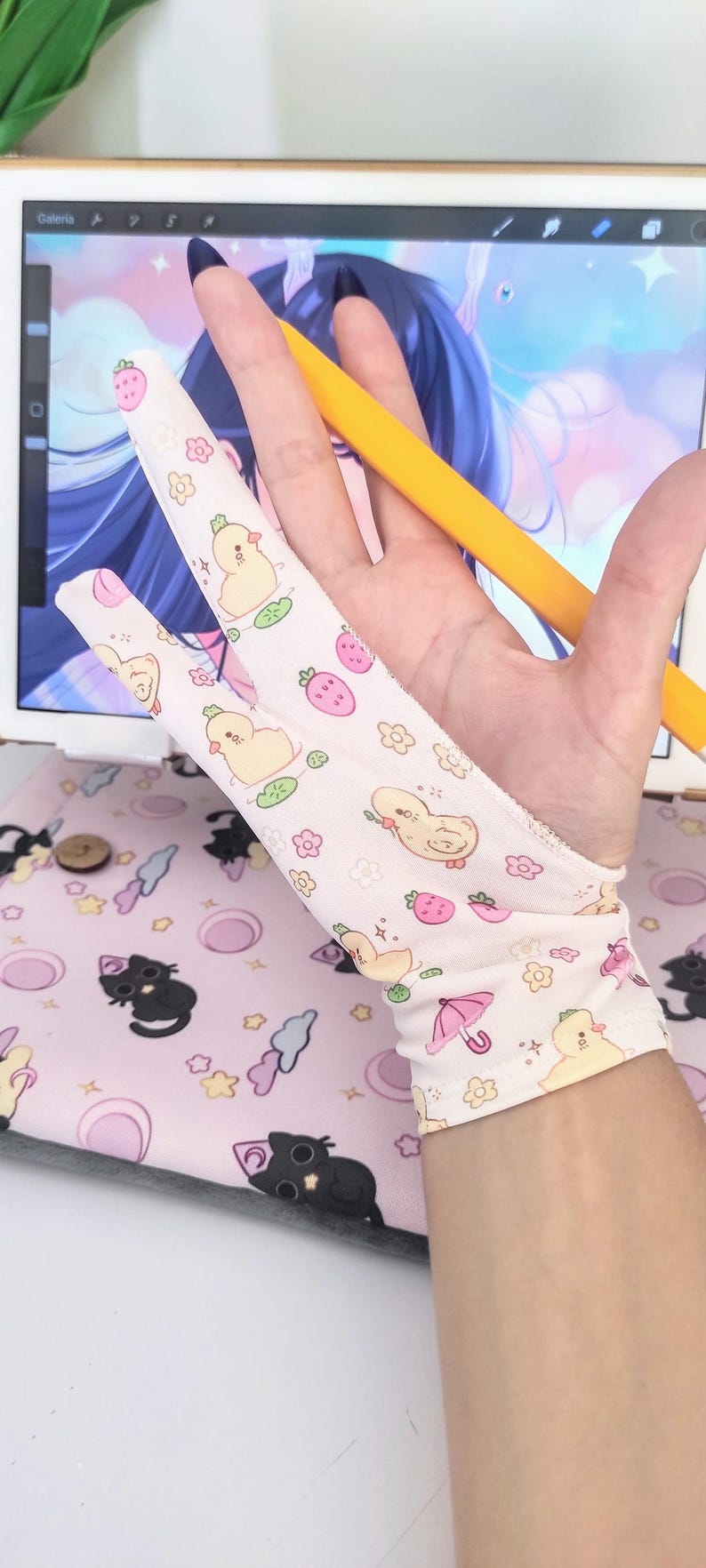May include: A light pink artist's glove with a pattern of yellow ducklings, strawberries, and flowers. A yellow stylus is held in the hand, with a digital drawing tablet in the background. The glove is designed for digital art.