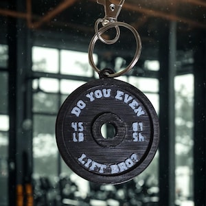 Puede incluir: Llavero de disco de pesas negro con el texto "DO YOU EVEN LIFT BRO?" en blanco. El disco de pesas muestra "45 LB" en cada lado. El llavero tiene un cierre y un anillo plateados.