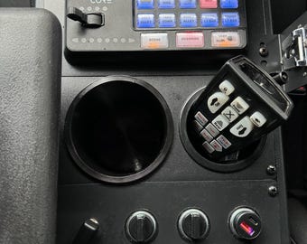 May include: Black control panel with the text "Whelen Core" and multiple buttons labeled with functions like "Wail", "Yelp", and "Horn". Includes a cup holder, a microphone, and various switches and dials.