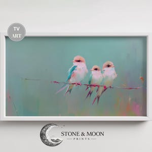 Op de afbeelding: Een ingelijste kunstdruk met drie pastelkleurige vogels die op een dunne tak zitten tegen een zachte, blauwgroene achtergrond. De vogels hebben roze, blauwe en gele accenten. De print is gelabeld met "TV ART".