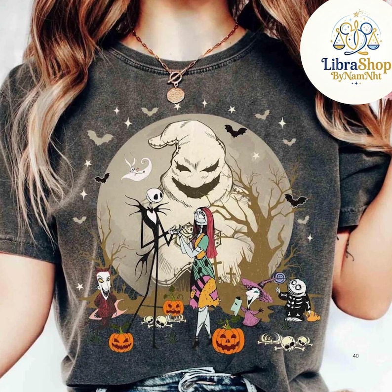 Może przedstawiać: Ciemnoszara koszulka z grafiką o tematyce Halloween. Projekt przedstawia Jacka Skellingtona, Sally i Oogie Boogie przed pełnią księżyca. Nietoperze, dynie i inne postacie dopełniają scenę. Koszulka ma efekt vintage.