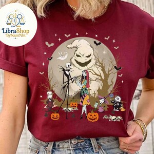 Może przedstawiać: Bordowa koszulka z grafiką o tematyce Halloween. Projekt zawiera Jacka Skellingtona, Sally i Oogie Boogie przed pełnią księżyca. Nietoperze, dynie i inne postacie dopełniają scenę. Logo LibraShop znajduje się w lewym g&oacute;rnym rogu.
