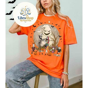 Może przedstawiać: Pomarańczowa koszulka z grafiką z filmu "Miasteczko Halloween". Projekt zawiera Jacka Skellingtona, Sally, Oogie Boogie i inne postacie. Koszulka ma okrągły dekolt i kr&oacute;tkie rękawy. Logo LibraShop jest widoczne w lewym g&oacute;rnym rogu.
