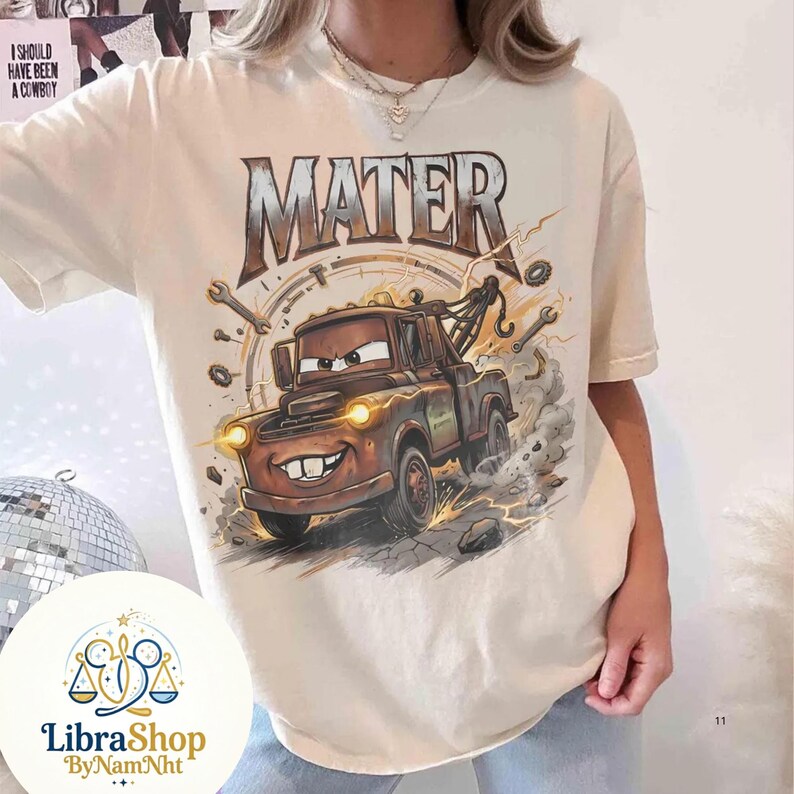 May include: Cream-colored t-shirt featuring a cartoon image of Mater from the movie Cars. The graphic includes the word "MATER" above the tow truck, along with wrenches and lightning bolts. The shirt has a relaxed fit.