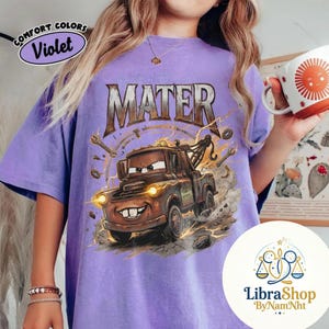 May include: Violet Comfort Colors t-shirt featuring a cartoon image of Mater from the movie Cars. The design includes the word "MATER" in a distressed font, along with tools and lightning bolts. The shirt also has the text "Comfort Colors" and "Violet".