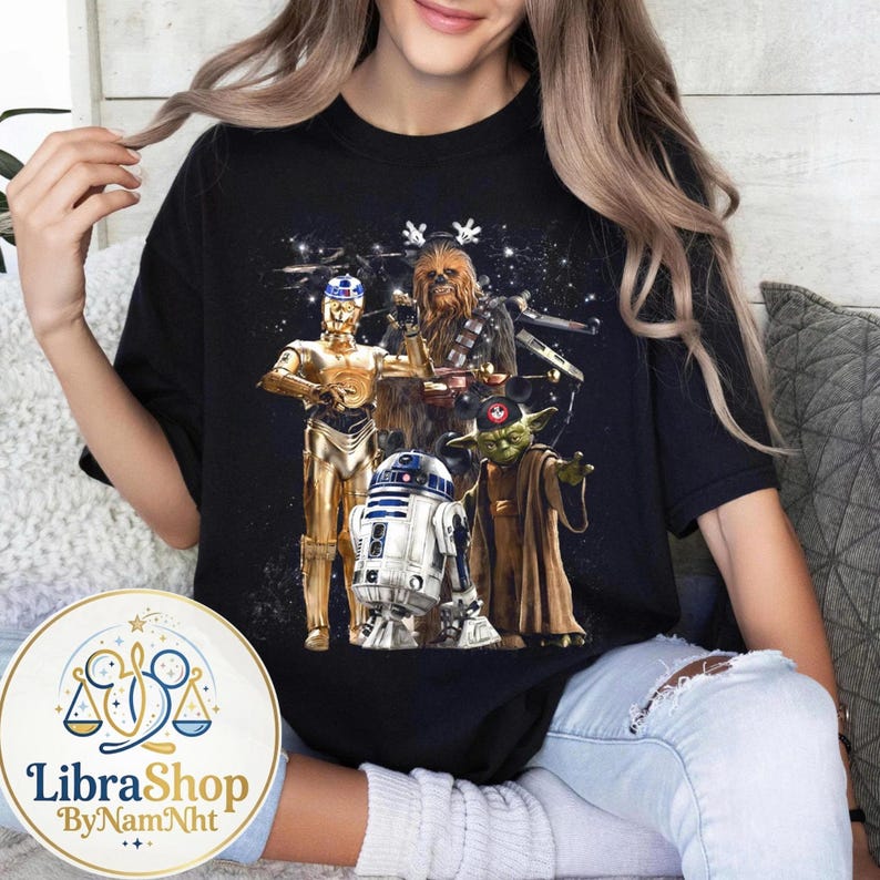 Może przedstawiać: Czarny t-shirt z grafiką Star Wars przedstawiającą C-3PO, Chewbaccę, R2-D2 i Yodę. Projekt zawiera gwiezdne tło i świąteczne elementy. Wygodny, codzienny element garderoby.