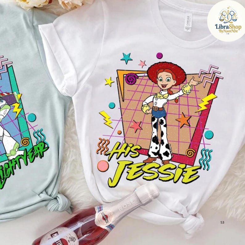 May include: White t-shirt featuring a cartoon image of Jessie from Toy Story, with the text "His Jessie". The design includes stars, lightning bolts, and a retro grid background. A second light blue t-shirt with a Buzz Lightyear design is also visible.
