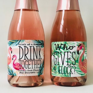 May include: Two bottles of pink-colored beverage with rose gold foil tops. Each bottle has a label with a flamingo illustration and text. One reads "Drink Together" and the other says "Who Gives a Flock?"