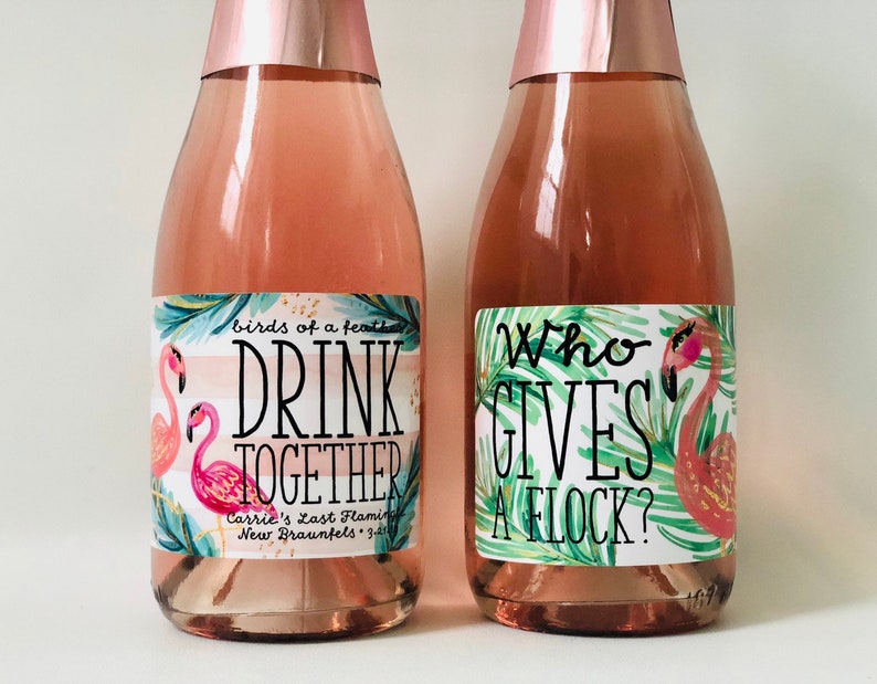 May include: Two bottles of pink-colored beverage with rose gold foil tops. Each bottle has a label with a flamingo illustration and text. One reads "Drink Together" and the other says "Who Gives a Flock?"
