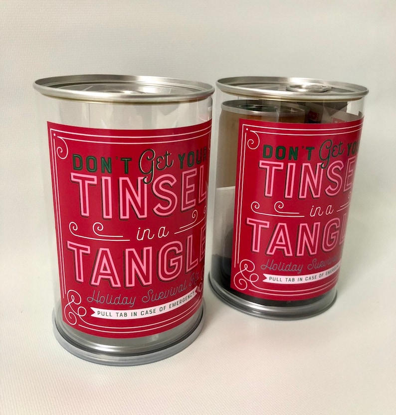 May include: Two clear plastic containers with silver lids and bases. Each container has a red label with the text "DON'T Get Your TINSEL in a TANGLE" in white and pink. The containers are for holiday survival.