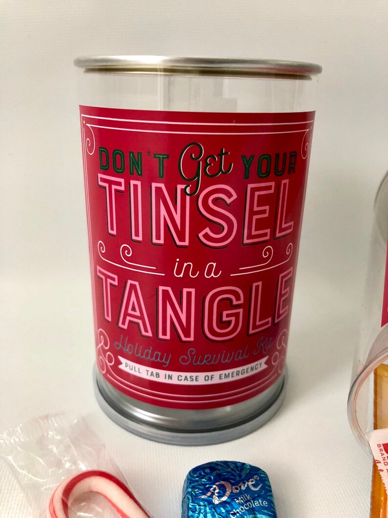 May include: A clear plastic container with a red label that reads "DON'T Get YOUR TINSEL in a TANGLE". The container is a holiday survival kit, with a pull tab for emergencies. Candy cane and chocolate are visible.