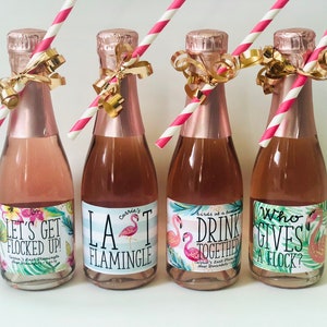 May include: Four mini champagne bottles with pink liquid, each adorned with a pink and white striped straw and gold ribbon. The labels feature tropical floral designs and phrases like "Let's Get Flocked Up!" and "LA Flamingle."
