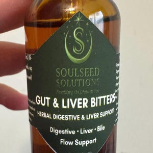 May include: An amber glass bottle containing liquid with a dark green diamond-shaped label. The label features the text Soulseed Solutions, Gut & Liver Bitters, Herbal Digestive & Liver Support, Digestive, Liver, Bile, Flow Support, and 1 fl oz (30 mL).