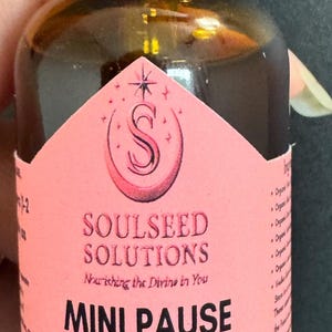 May include: A 1 fl oz amber glass dropper bottle with a black cap and a pink diamond-shaped label. The label features the text SOULSEED SOLUTIONS, Nourishing the Divine in You, MINI PAUSE, WOMEN'S WELLNESS HERBAL BLEND, Hormonal Balance, Hot Flash Support, Emotional Wellness, and 1 fl oz (30 mL).
