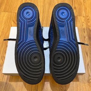May include: A pair of blue and black sneakers with a textured sole. The soles are black with a blue center and the Nike logo. The sneakers are on top of a white box.