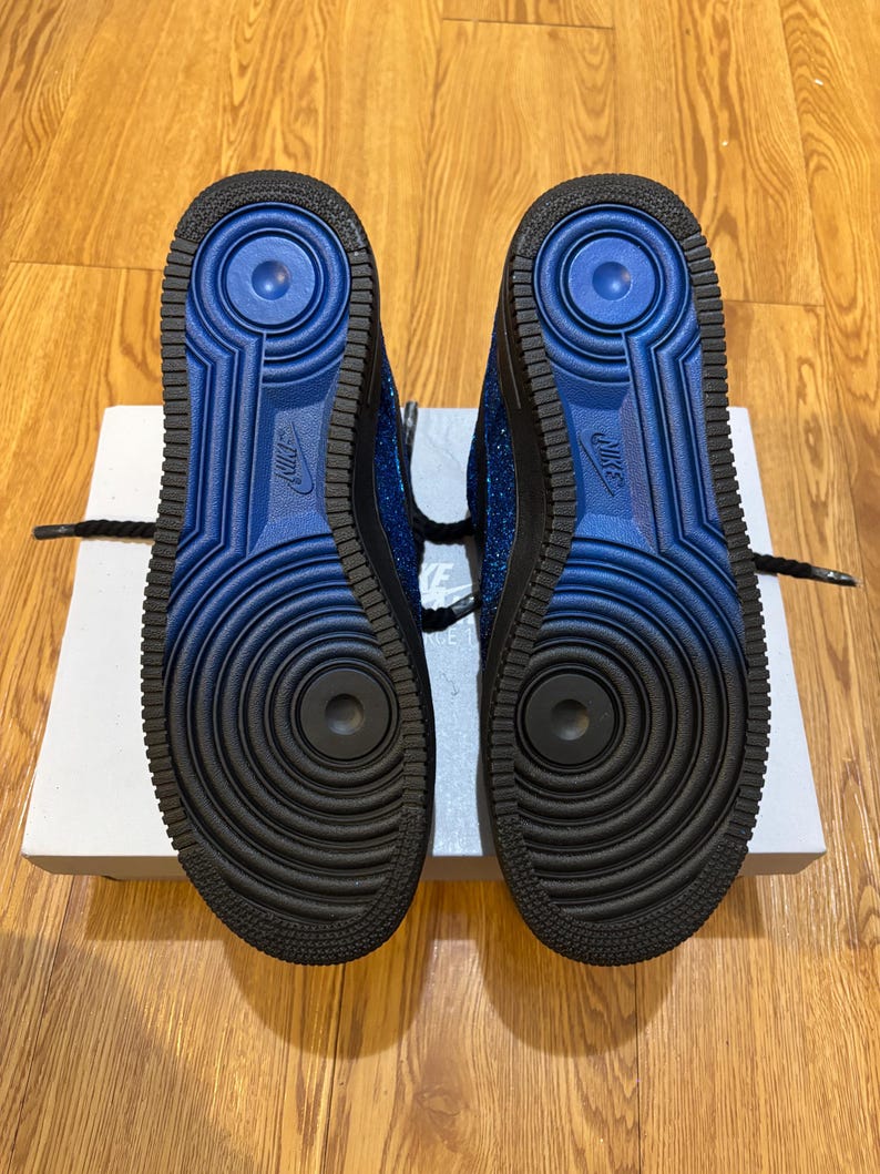 May include: A pair of blue and black sneakers with a textured sole. The soles are black with a blue center and the Nike logo. The sneakers are on top of a white box.