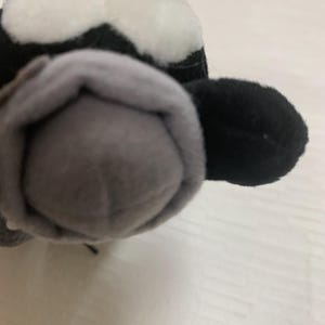 Op de afbeelding: Een pluche speelgoed in de vorm van een panda. De panda heeft een zwart-witte kop met kleine zwarte ogen en een grijze neus. Het oor van de panda is zwart. Het speelgoed is gemaakt van zacht, pluche materiaal.