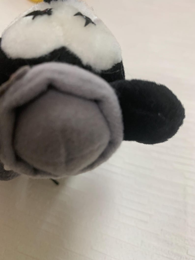 Op de afbeelding: Een pluche speelgoed in de vorm van een panda. De panda heeft een zwart-witte kop met kleine zwarte ogen en een grijze neus. Het oor van de panda is zwart. Het speelgoed is gemaakt van zacht, pluche materiaal.