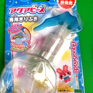 May include: A clear plastic spray bottle with a blue trigger, packaged on a blue and green card. The card features Japanese text and a colorful bead art design of a rabbit. The package is labeled "Aquabeads".