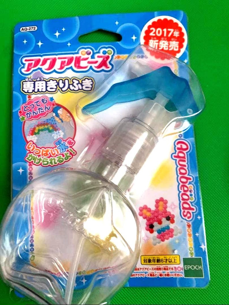 May include: A clear plastic spray bottle with a blue trigger, packaged on a blue and green card. The card features Japanese text and a colorful bead art design of a rabbit. The package is labeled "Aquabeads".