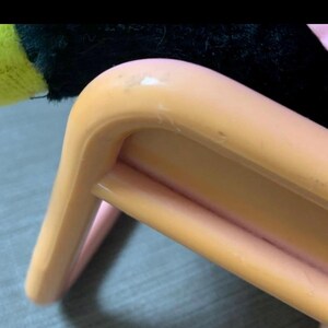 May include: Close-up of a light orange plastic chair leg. The chair leg has a curved design with a rounded top and a supporting bar. The chair appears to be made of plastic and has a smooth surface.