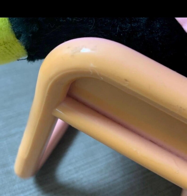 May include: Close-up of a light orange plastic chair leg. The chair leg has a curved design with a rounded top and a supporting bar. The chair appears to be made of plastic and has a smooth surface.