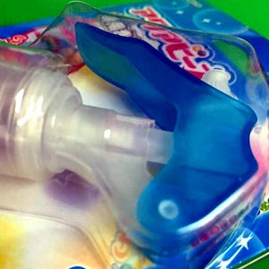 May include: A close-up of a baby bottle with a blue handle and a clear nipple. The bottle is partially visible, with the focus on the blue handle and the packaging. The packaging has a blue and white design with the word "baby" visible.