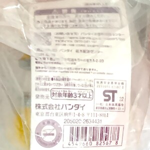 May include: A white rectangular product information tag encased in clear plastic packaging. The tag features black Japanese text, a barcode, the Bandai company name, a safety warning symbol, and the ST 22 safety certification mark for toys.