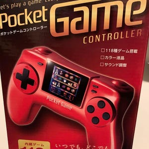 Pode incluir: Controlador Pocket Game vermelho com um pequeno ecr&atilde; que exibe gr&aacute;ficos de jogos. O controlador tem um D-pad em forma de cruz, bot&otilde;es e o texto "Pocket Game" na frente. A caixa diz "Let's play a game. Everybody has fun."