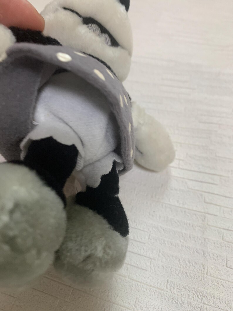 Op de afbeelding: Een zacht pandabeerspeelgoed met zwart-witte vacht, gekleed in een grijze jurk met witte stippen. De poten van de beer zijn grijs en zwart. Een schattig en knuffelbaar speelgoed voor kinderen.