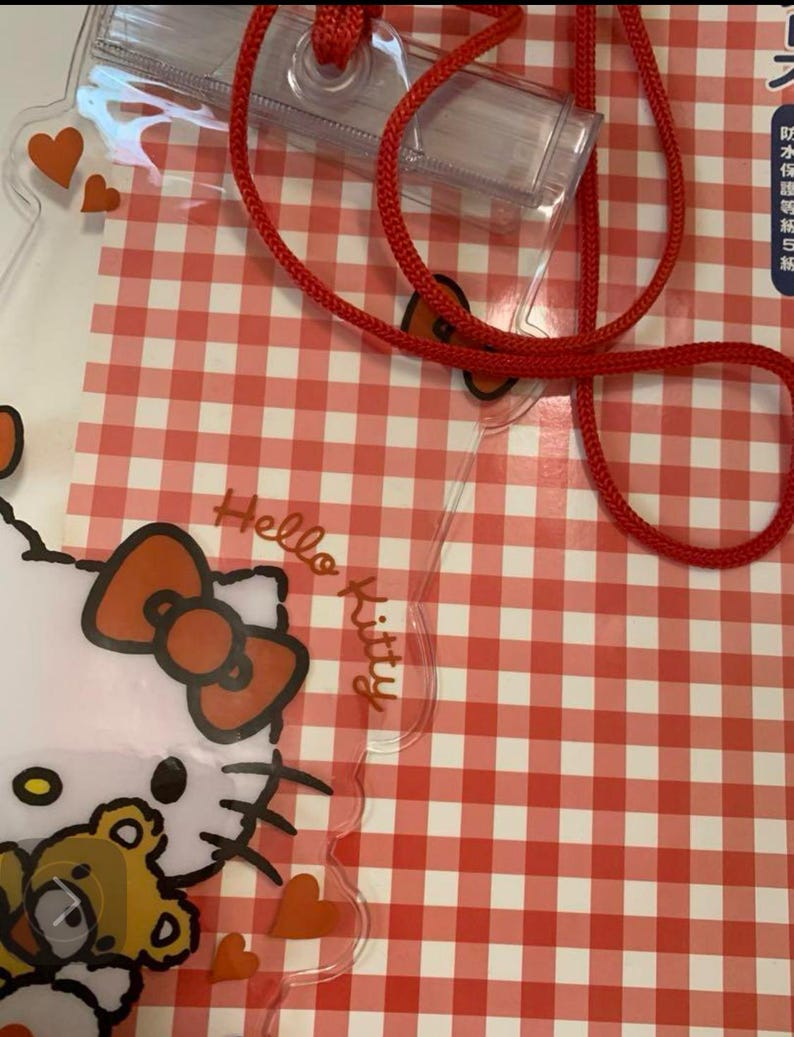Pode incluir: Cord&atilde;o Hello Kitty de pl&aacute;stico transparente com um cord&atilde;o vermelho e um porta-identifica&ccedil;&otilde;es transparente. O cord&atilde;o apresenta um design Hello Kitty com um la&ccedil;o vermelho e um ursinho de pel&uacute;cia. O fundo &eacute; um padr&atilde;o xadrez vermelho e branco.