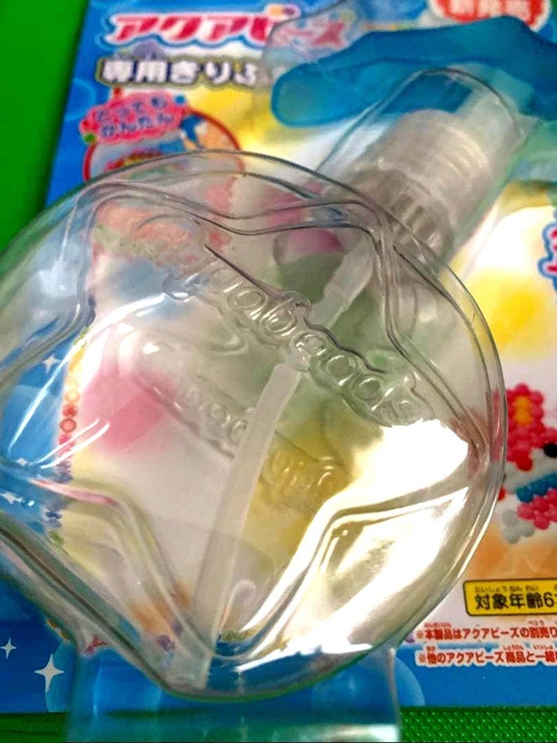 May include: A clear plastic spray bottle with a white nozzle and a clear, rounded container. The bottle is partially filled with a colorful liquid. Japanese text is visible on the packaging.