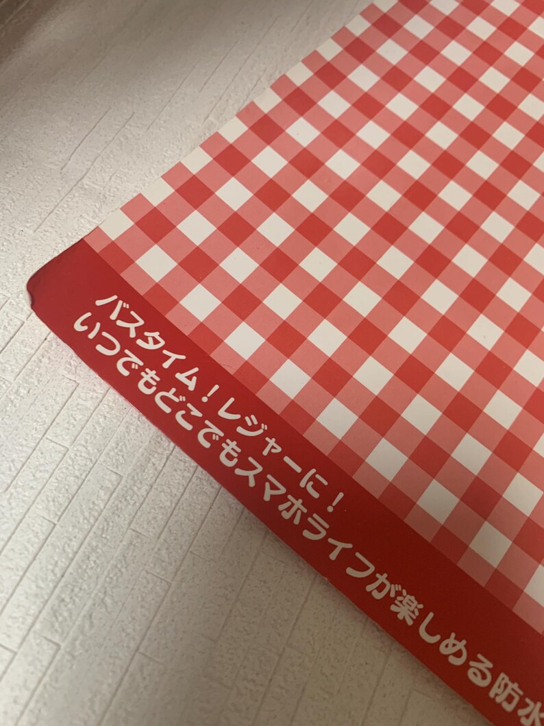 Pode incluir: Padr&atilde;o xadrez vermelho e branco em um objeto retangular. Texto japon&ecirc;s branco vis&iacute;vel em fundo vermelho. O texto diz: "Hora do banho! Lazer! Aproveite sua vida de smartphone em qualquer lugar!"